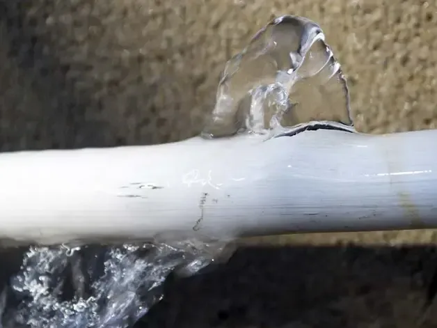 Water spraying from a split in a white plastic supply pipe