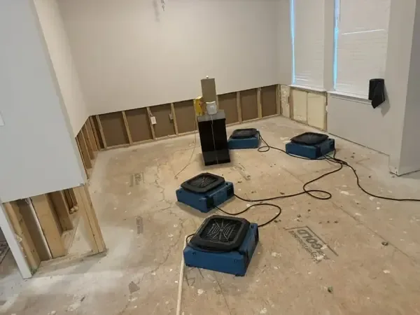 Several air movers on a bare floor beside walls with lower drywall removed