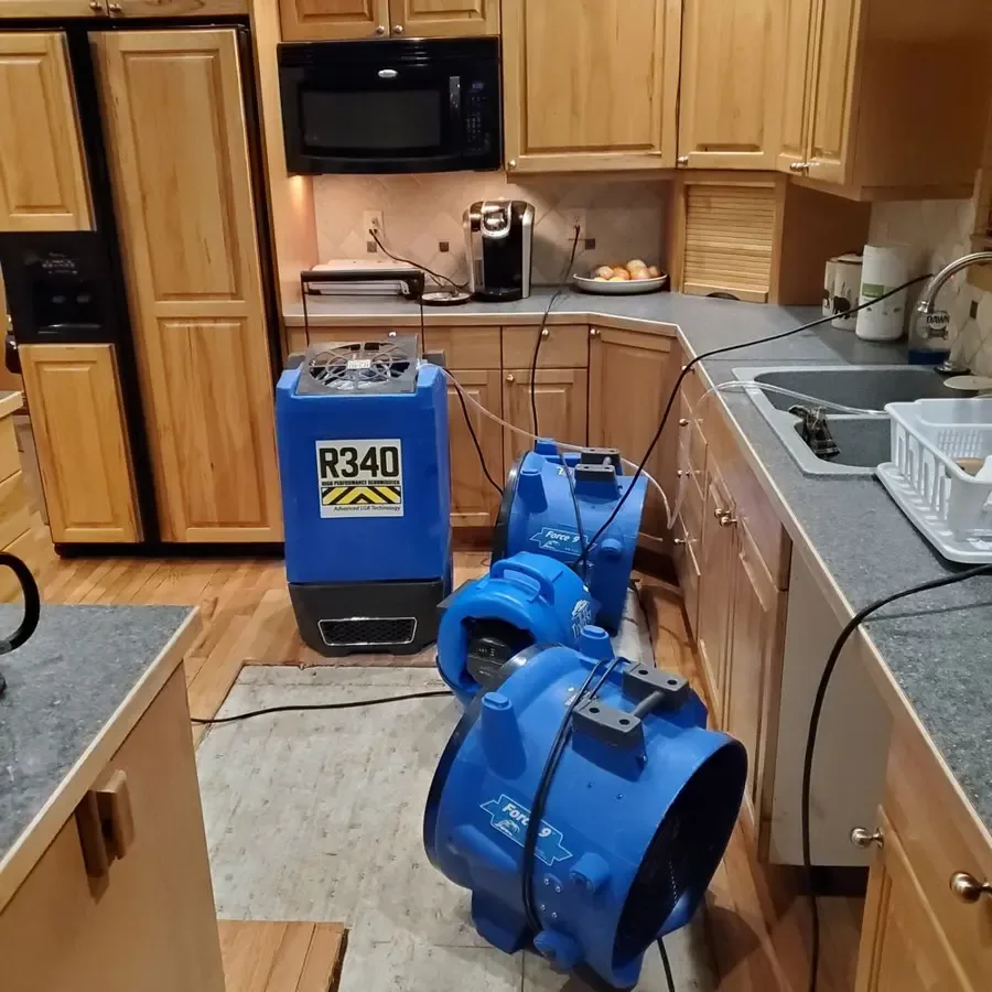Blue air movers surround a dehumidifier positioned across the floor of a kitchen