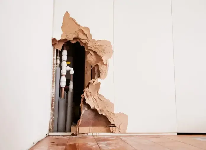 Wall opened around supply plumbing beside a wet wood floor