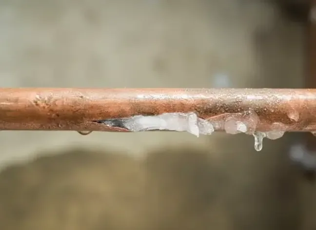 A copper pipe split along its underside with ice around the opening
