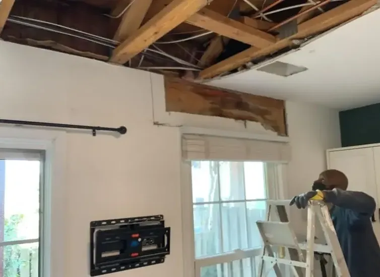 Worker on a ladder below a ceiling opened to expose wet roof framing