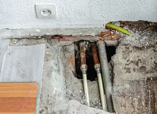 Floor opened through concrete to expose several copper pipes near the base of a wall