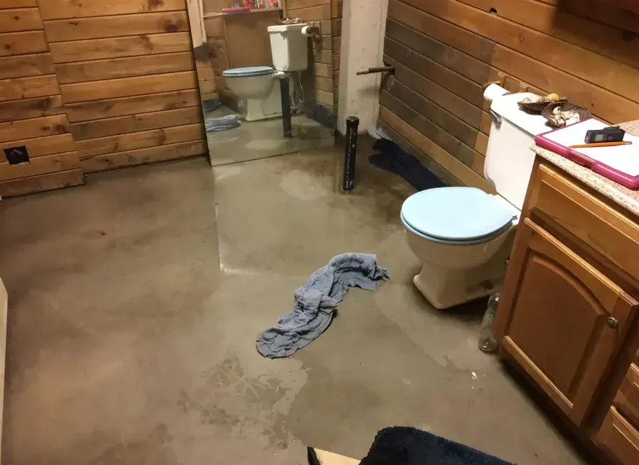 Water across a bathroom floor beside a toilet and wooden vanity